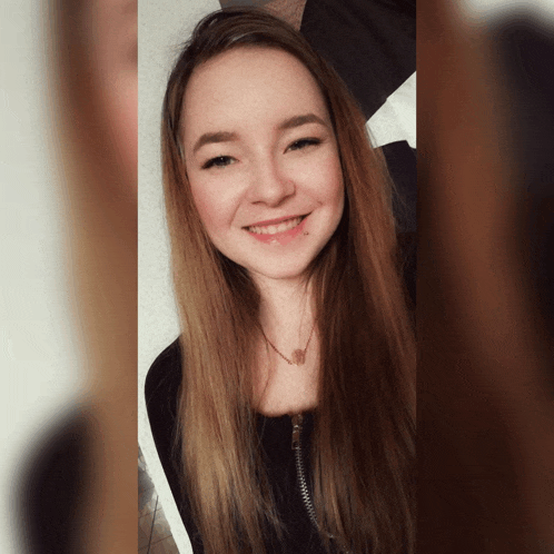 a woman with long brown hair is smiling and wearing a black shirt