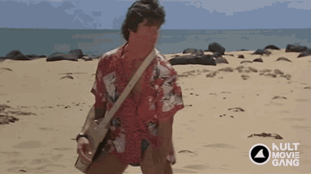 a man in a hawaiian shirt is walking on a beach with a kult movie gang logo in the corner