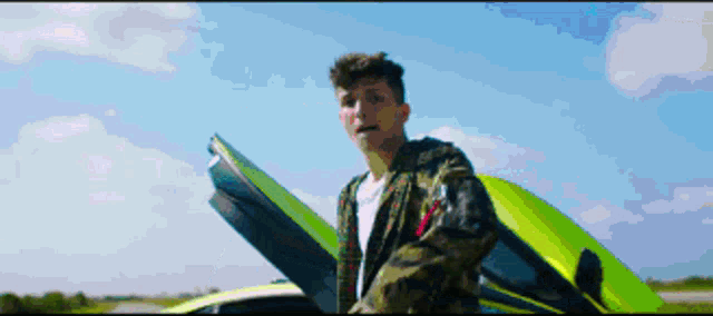 a man in a camo jacket stands next to a green sports car
