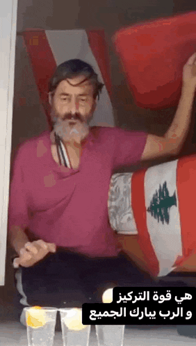 a man in a pink shirt is sitting in front of a flag and drinking a drink with lemon slices