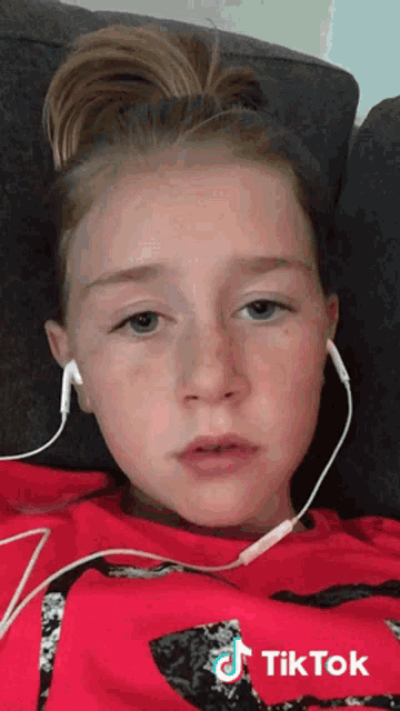 a young girl wearing headphones and a red shirt has a tiktok logo on her shirt