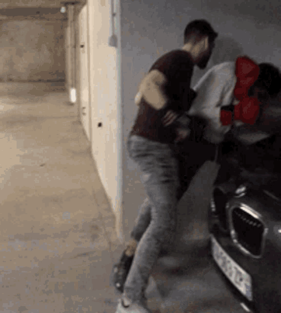 a man is pushing another man into a car with a license plate that says ' rb ' on it