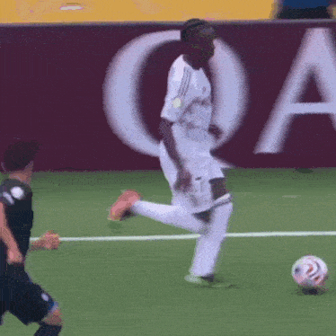 a soccer player kicking a ball in front of a sign that says qa