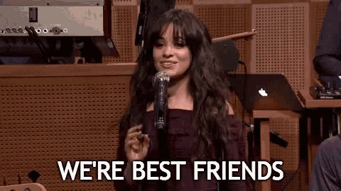 a woman is singing into a microphone with the words we 're best friends written on the screen behind her .