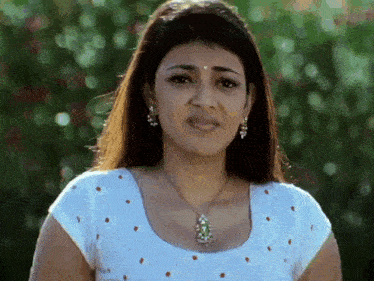 a woman wearing a white top and a necklace is looking at the camera