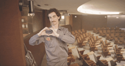 a man making a heart shape with his hands in front of empty auditorium seats