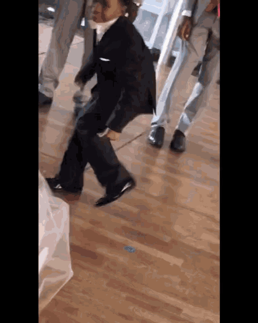 a young boy in a tuxedo is dancing on a wooden floor
