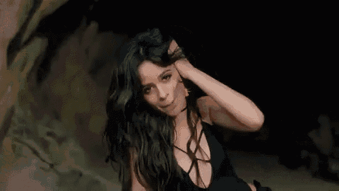 a woman in a black dress is touching her hair in a dark cave .