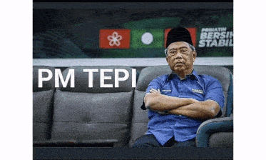 a man in a blue shirt is sitting on a couch with his arms crossed in front of a sign that says pm tep