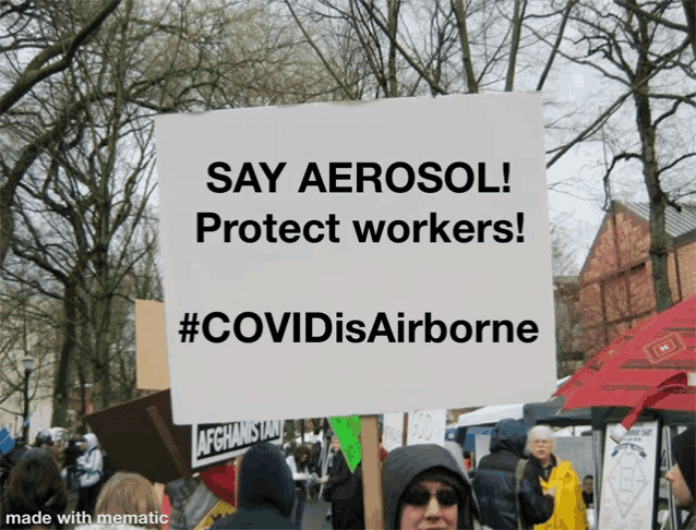 a protester holds a sign that says say aerosol protect workers