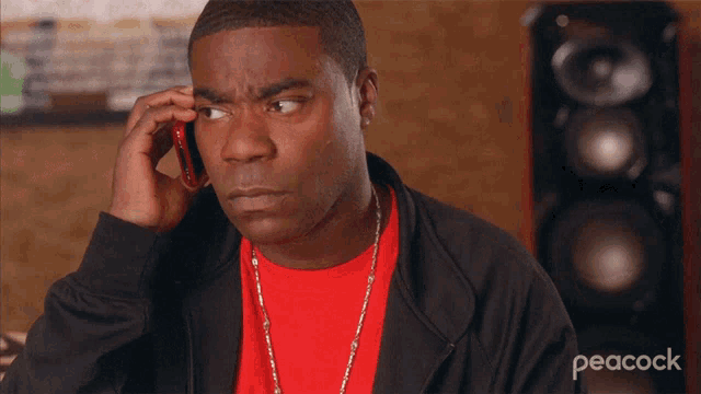 a man in a red shirt is talking on a cell phone with peacock written on the bottom