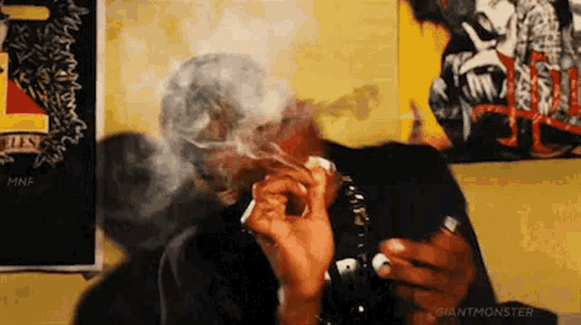 a man is smoking a cigarette in front of a wall with a painting on it .