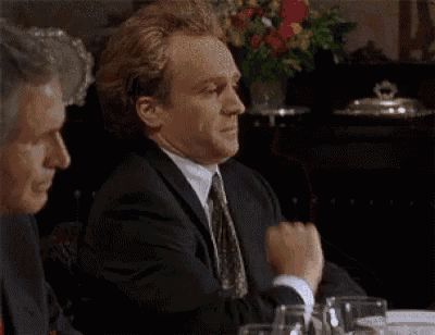 a man in a suit and tie is sitting at a table with glasses of wine .