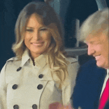 a woman in a trench coat is smiling next to a man in a suit .