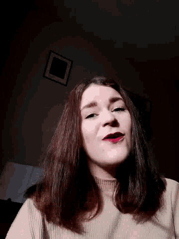 a woman wearing red lipstick and a white sweater looks at the camera