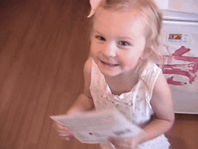 a little girl is holding a piece of paper in front of a refrigerator