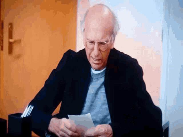 a man with glasses is sitting at a table looking at a piece of paper