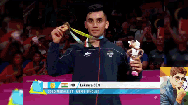 a man in a blue jacket is holding a gold medal and a stuffed animal