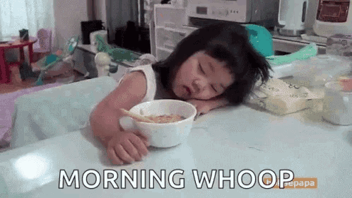 a little girl is sleeping at a table with a bowl of cereal in front of her .