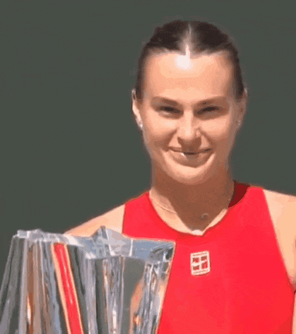 a woman in a red tank top is smiling while holding a trophy .