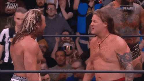 two wrestlers are standing next to each other in a wrestling ring in front of a crowd .
