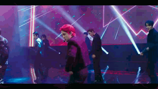 a group of men are dancing on a stage in front of a purple and red background .
