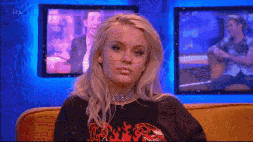 a blonde woman is sitting on a yellow couch in front of a television .