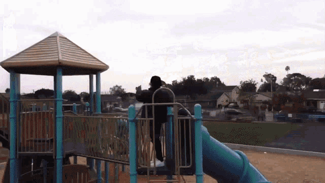 a person riding a slide at a playground with a gazebo in the background