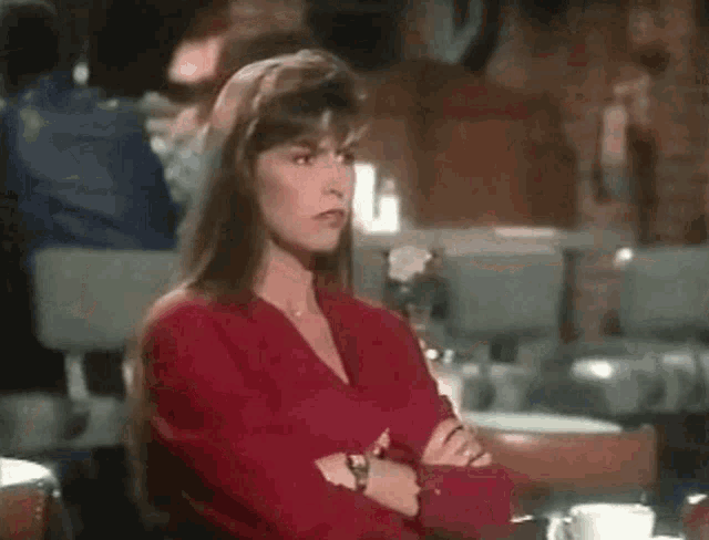 a woman in a red shirt is sitting in a chair with her hands folded and her mouth open .