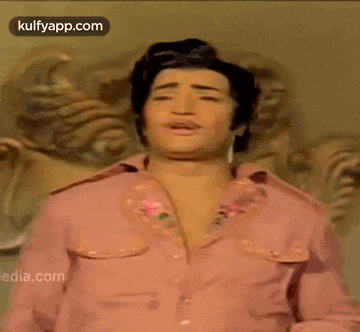 a man in a pink shirt is standing in front of a statue and making a face .