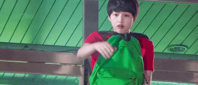 a young boy is carrying a green backpack while wearing a red shirt .