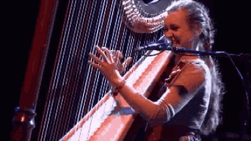 a woman is singing into a microphone while playing a harp