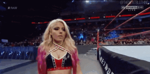 a woman is standing in a wrestling ring wearing a pink and red top .