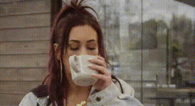 a woman is drinking a cup of coffee while sitting in front of a window .