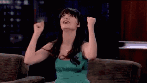 a woman in a green dress is sitting on a couch with her arms in the air and smiling .