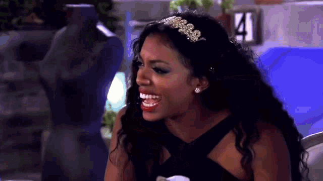 a woman in a black dress and tiara is laughing while sitting on a couch .