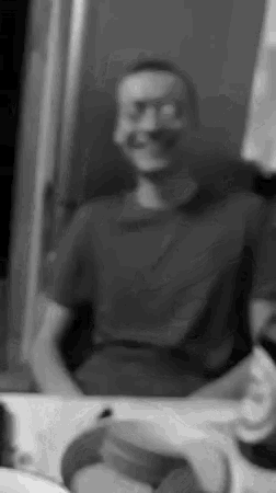 a man is smiling in a black and white photo while looking at himself in the mirror .