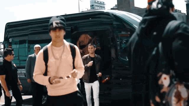 a man in a pink sweater stands in front of a van that has the number 19 on it