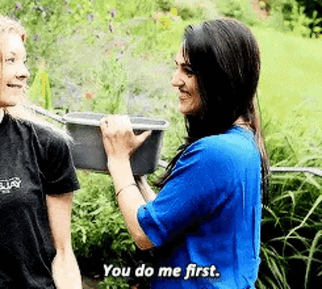 a woman in a blue shirt is talking to another woman in a black shirt while holding a bucket .
