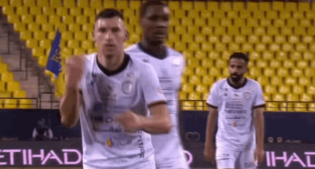 a group of soccer players are running on a field in front of a yellow stadium .