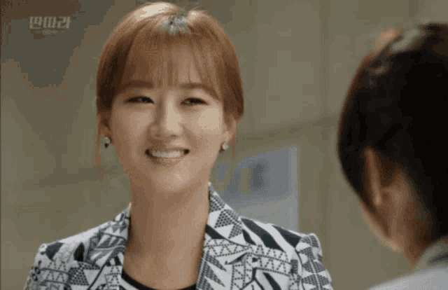 a woman in a black and white jacket smiles in front of a sign that says ' a ' on it