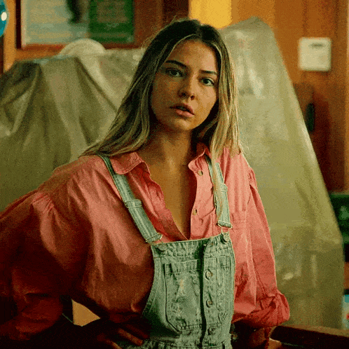a woman is wearing overalls and a pink shirt .