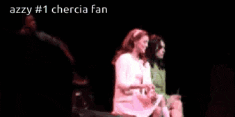 two women are sitting on a stage in a dark room with the words azzy # 1 chercia fan above them