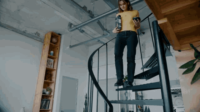 a woman in a yellow shirt is standing on a spiral staircase