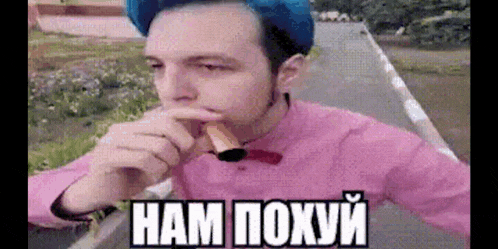a man wearing a pink shirt and a blue hat is eating a sandwich .
