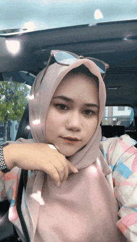 a woman wearing a hijab and sunglasses takes a selfie in a car