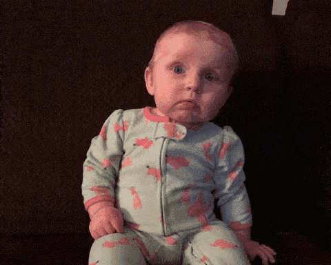 a baby in a giraffe pajamas is making a sad face .