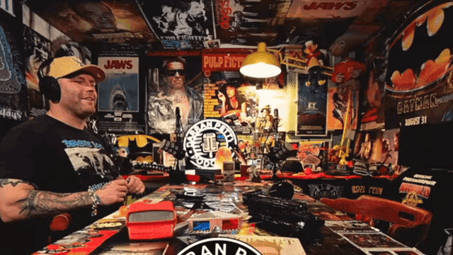a man wearing headphones sits at a table with a jaws poster on the wall