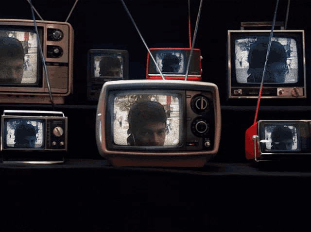 a row of old televisions with a man 's face on the screens