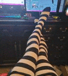 a person wearing black and white striped socks is sitting in front of a computer monitor .